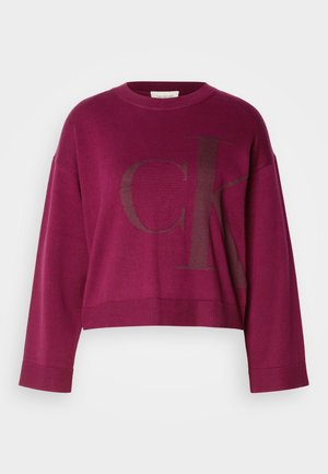 Bordó cropped pulóver hosszú ujjal, nagy sötétszürke 'CK' logóval az elején és bordázott mandzsettával. Puha kötött anyag.