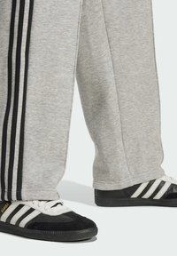 Šedé tepláky s čiernymi pruhmi a čierne tenisky Adidas Samba s bielym prúžkovaním a gumovými podrážkami.