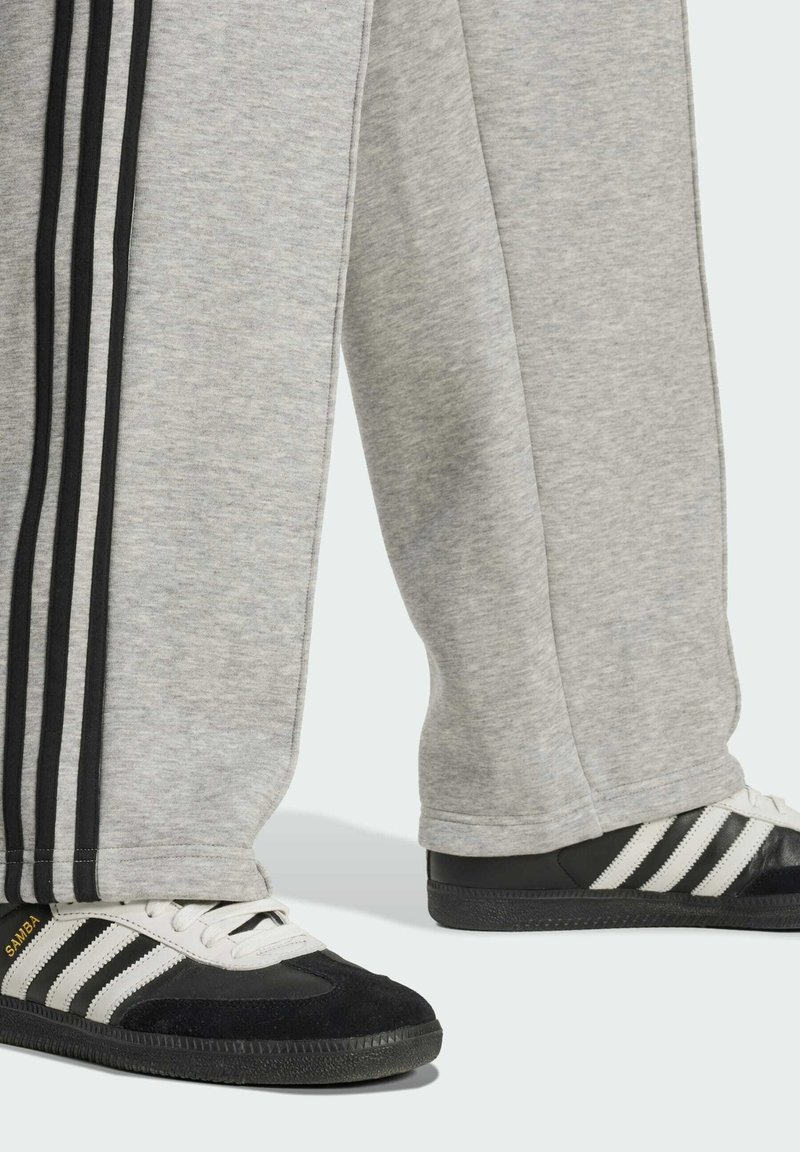 Pantalones de chándal grises con rayas negras y zapatillas Adidas Samba negras con un patrón de rayas blancas y suelas de goma.