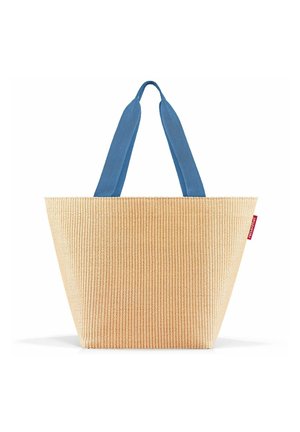 Sac tote avec une texture tissée beige clair, design effilé et poignées en tissu bleu. Présente une petite étiquette logo rouge sur le côté.