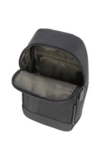 Črn nahrbtnik iz blaga z gladko teksturo; zgornje zadrgo se odpre in razkrije notranjost z sivim podlogom ter eno dodatno zadrgo.