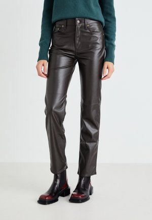 Pantaloni in finta pelle marrone con una silhouette aderente, vita alta e un leggero lucido. Abbinati a stivaletti neri e bordeaux.