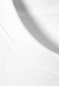 Gros plan sur un col rond côtelé blanc d'un t-shirt en coton blanc uni, montrant la texture du tissu et les coutures.