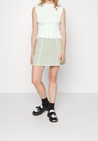 Bílý nařasený top s volánovým lemem, doplněný světle zelenou áčkovou sukní se scalloped okraji a lemováním. Černé boty s bílými akcenty.