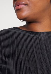 Tessuto plissettato nero con una superficie liscia, caratterizzato da righe orizzontali e un colletto rotondo, mostrato da vicino nella zona del colletto.