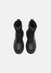 Sorte skinn ankle boots med en teksturert finish, snøring foran og glidelås på siden. Tykk gummisåle med et robust mønster.