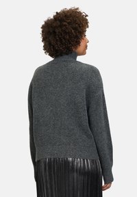 Grauer, gestrickter Pullover mit hohem Kragen und lockerem Schnitt, ausgestattet mit gerippten Ärmeln und einem gerippten Saum. Kombiniert mit einem metallischen, plissierten Rock.