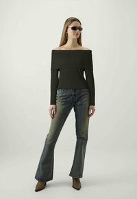Black off-the-shoulder top with ribbed texture, paired with faded blue flared jeans and brown pointed-toe heels. Model wearing sunglasses.