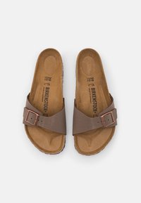 Sandales Birkenstock marron avec une seule sangle réglable et une boucle couleur cuivrée, dotées d'une semelle intérieure en liège contournée et d'une semelle extérieure texturée.