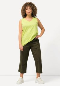 V-ringad, ärmlös limegrön linne med vita ränder, parat med olivgröna capribyxor och vita sneakers.