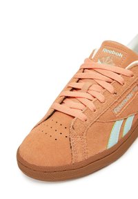 Narancs suede Reebok Classic sneaker illeszkedő fűzőkkel, perforált orral, fehér logós csíkokkal és gumi talppal fehér hátt�éren.