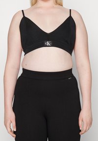 Mustaprasetti V-koteloisella muotoilulla, ribbikuvioinnilla ja logonauhadetaililla. Yhdistetty korkeavyötäröisten mustien housujen kanssa, jotka yhdessä tarjoavat sileän siluetin.