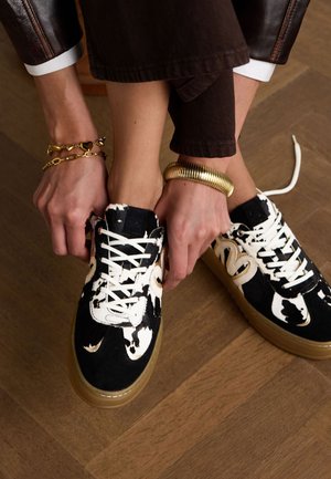 Zwart-witte gestreepte sneakers met vetersluiting en een chunky, transparante zool. Bruine houten vloer zichtbaar eronder.