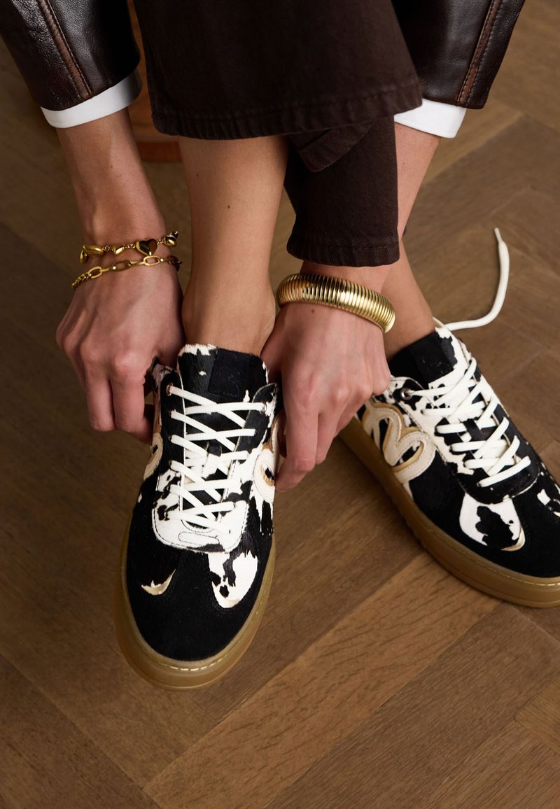 Zwart-witte gestreepte sneakers met vetersluiting en een chunky, transparante zool. Bruine houten vloer zichtbaar eronder.