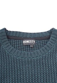 Mörkblå stickad tröja med texturerat mönster, rund halsringning och kontrasterande turkosa accenter. Märket säger "ÄRLIGHET REGEL" och storlek L.