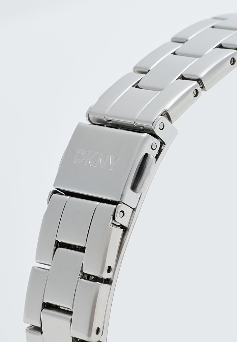 Bracelet de montre en acier inoxydable avec des maillons connectés, finition Polie et fermoir avec logo "DKNY" gravé.