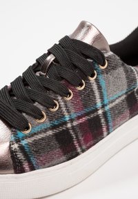 Zapatillas de cuadros con un patrón en gris, negro y burdeos, acentos metálicos, cordones negros y ojales dorados sobre una suela de goma blanca.