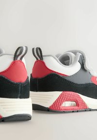 Grå og røde atletiske sko med mesh- og ruskindsoverdel, teksturerede detaljer, trækflapper og synlig luftdæmpning i sålen.