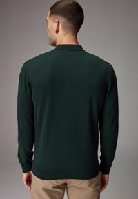 Suéter tipo polo de manga larga en tejido de punto verde oscuro. Cuenta con un dobladillo y puños acanalados, además de un diseño de cuello clásico. Vista trasera simple y elegante.