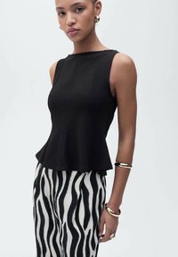 Haut péplum noir en tissu lisse, associé à un pantalon rayé zèbre noir et blanc. Accents notables de bijoux en ton doré.