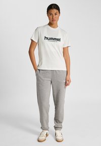 Hvid bomulds t-shirt med sort "hummel" logo og grå bomulds sweatpants. Skoen har en cremegul farve med sorte striber og gummisål.