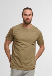 Oliva grön t-shirt med korta ärmar gjord av mjukt tyg, med en bröstficka med en liten accentdetalj. Klassisk rund halsringning.
