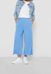 Light blue, wide-leg pants with an elastic waistband and side pockets, paired with a white t-shirt and light denim jacket. White sneakers.