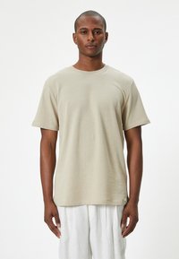 T-shirt beige a maniche corte realizzato in tessuto morbido, con collo rotondo, vestibilità rilassata e una leggera trama. Etichetta nella parte inferiore.