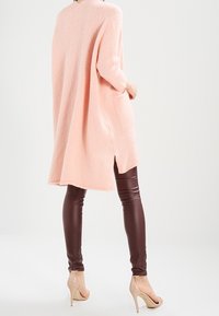 Oversized pink knit sweater with side slits, paired with brown faux leather leggings and nude high heels. Soft texture and casual design.