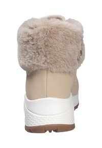 Calzado beige con un puño de piel de pelo suave en el tobillo, suela blanca, entresuela texturizada y detalle de botón en el lateral. Diseñado para comodidad y calidez.