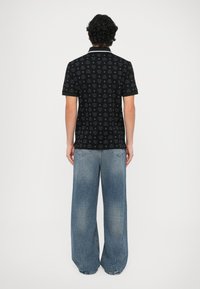 Camiseta polo negra con un sutil patrón de logotipos en toda la prenda, contrastada por un cuello blanco, combinada con jeans de tono azul claro y corte holgado.