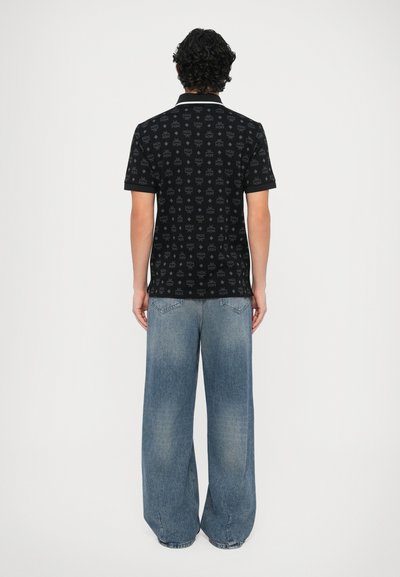 Polo preta com padrão de logotipo sutil em toda a peça, contrastada por uma gola branca, combinada com jeans azul claro de corte folgado.