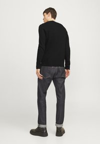 Svart ribbad tröja med långa ärmar, matchad med mörka denimjeans som har uppkavlade muddar och subtila sömmar. Bruna stövlar fulländar looken.