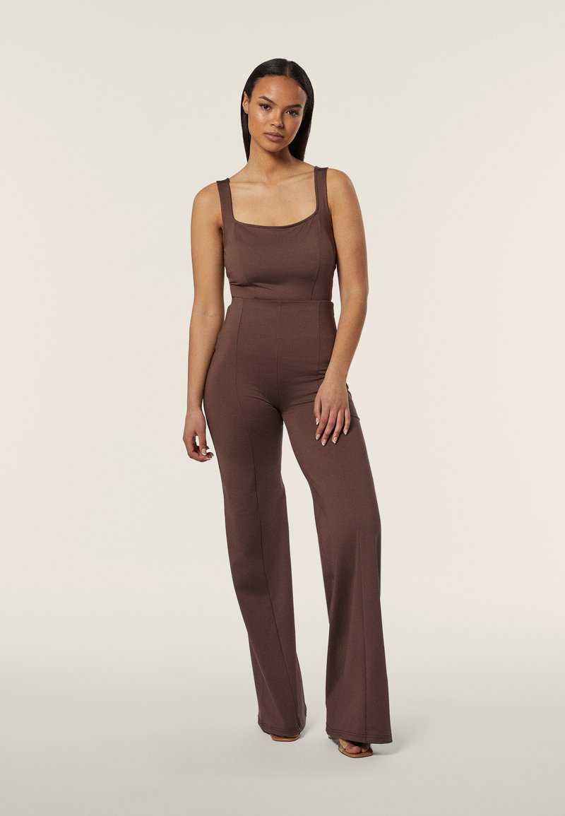 Jumpsuit marrone attillato con scollatura quadrata, spalline larghe e gambe svasate, realizzato in materiale liscio, con design senza cuciture e dettagli minimi.