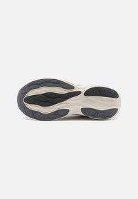 Semelle de chaussure avec un design ondulé comprenant des textures variées, majoritairement noire avec des accents crème, et des crampons arrondis pour l'adhérence.