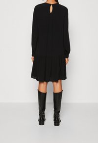 Vestido negro con mangas largas, diseño en capas, detalle de escote en forma de llave en la parte posterior y tejido suave. Combinado con botas negras hasta la rodilla.