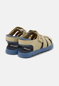 Beżowe sandały z niebieskimi akcentami, z otwartym designem, wieloma paskami i zapięciem na rzep. Miękka wyściółka wewnętrzna i teksturowana podeszwa.