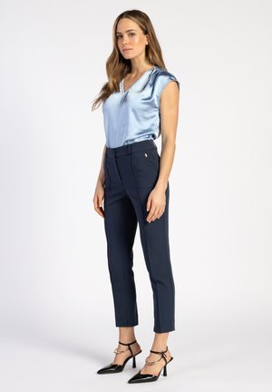 Blouse en satin bleu clair avec un col en V et des manches courtes, associée à un pantalon navy ajusté et des talons noirs à bout pointu avec des brides à la cheville.