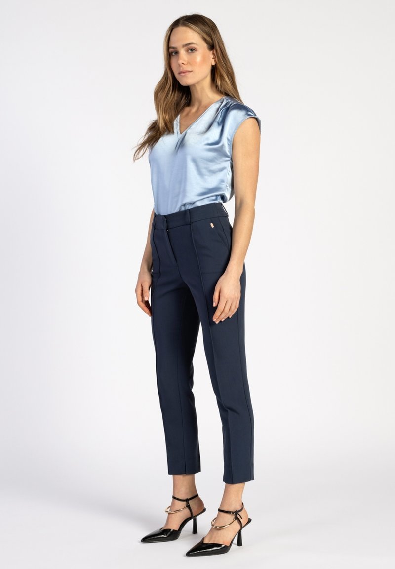 Lichtblauwe satijnen blouse met een V-hals en korte mouwen, gecombineerd met op maat gemaakte marineblauwe broek en zwarte puntige hakken met enkelbandjes.