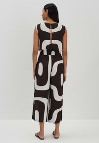 Mouwloze jumpsuit in zwart en wit met abstracte patronen. Heeft een getailleerde taille en een open rugdetail met een sleufuitsnijding.