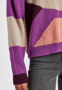 Maglione lavorato a maglia con una trama a costine che presenta audaci motivi geometrici in viola, beige e pesca, con polsini color viola scuro.
