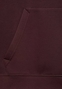 Burgundowa bluza z fakturowanej tkaniny. Posiada kieszeń kangurzą oraz detale szwów wokół kieszeni i dołu.