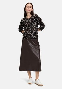 Czarny kardigan z białym i brązowym abstrakcyjnym wzorem, zestawiony z długą brązową skórzaną spódnicą i białymi butami z jasnobrązową podeszwą.