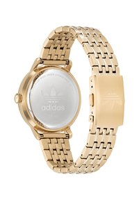 Montre en acier inoxydable doré avec un bracelet en maille. Boîtier rond avec un fond en verre affichant le logo adidas. Fermeture à clip.