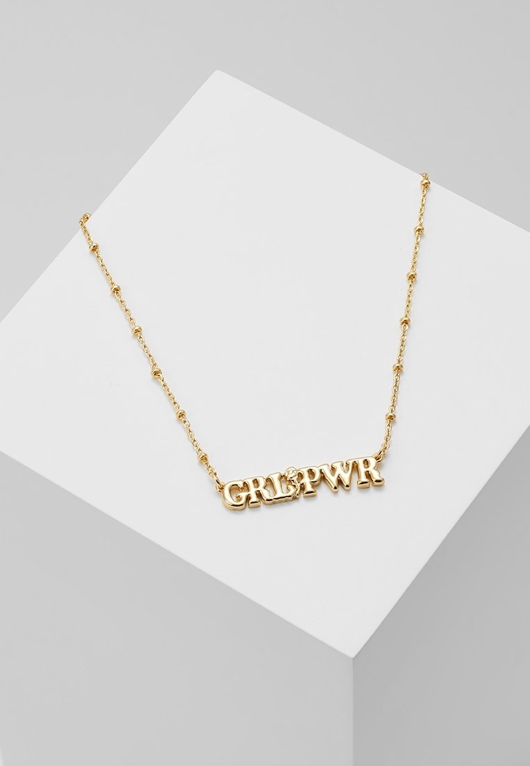 Collier chaîne en or avec les lettres du pendentif "GRL PWR" affichées sur une surface géométrique blanche.