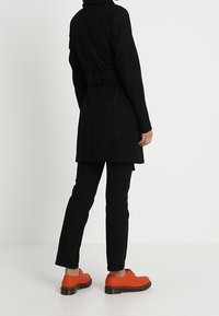 Černý kabát s páskem a vysokým límcem, nošený přes černé kalhoty. Charakterizován oranžovými botami s kulatou špičkou a kontrastní podrážkou.