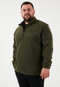 Olivengrøn fleece-pullover med kvart-lynlås i halsen. Har lange ærmer og et lille logo på brystet. Blødt, struktureret stof.