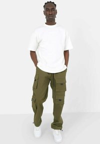 Witte oversized t-shirt gecombineerd met olijfgroene cargo-broek met meerdere zakken en ritsen, aangevuld met witte sneakers.