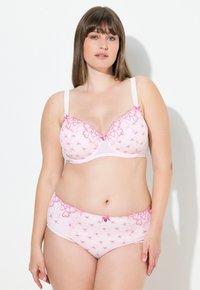 Ruusukuvioinnilla varustettu pitsireunainen vaaleanpunainen rintaliivi, jossa on säädettävät olkaimet, yhdistettynä samanlaisiin kuviin ja yksityiskohtiin sisältäviin poikashortsit.