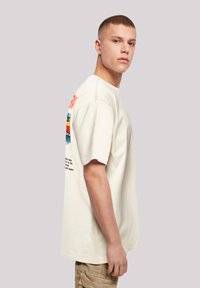Cream cotton T-shirt with short sleeves, featuring colorful graphic prints on the back, and a relaxed fit. Seam detailing is visible.